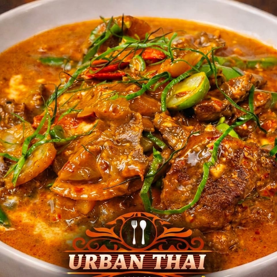 Bowl of rich Thai red curry with meat, vegetables, chilies, and fresh herbs, labeled Urban Thai.