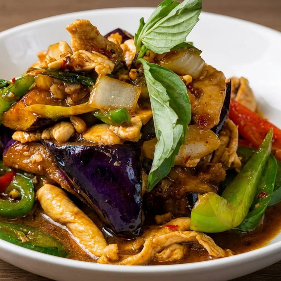 Thai-style stir-fry with chicken, eggplant, peppers, onions, cashews, and basil in a savory sauce on a white plate.