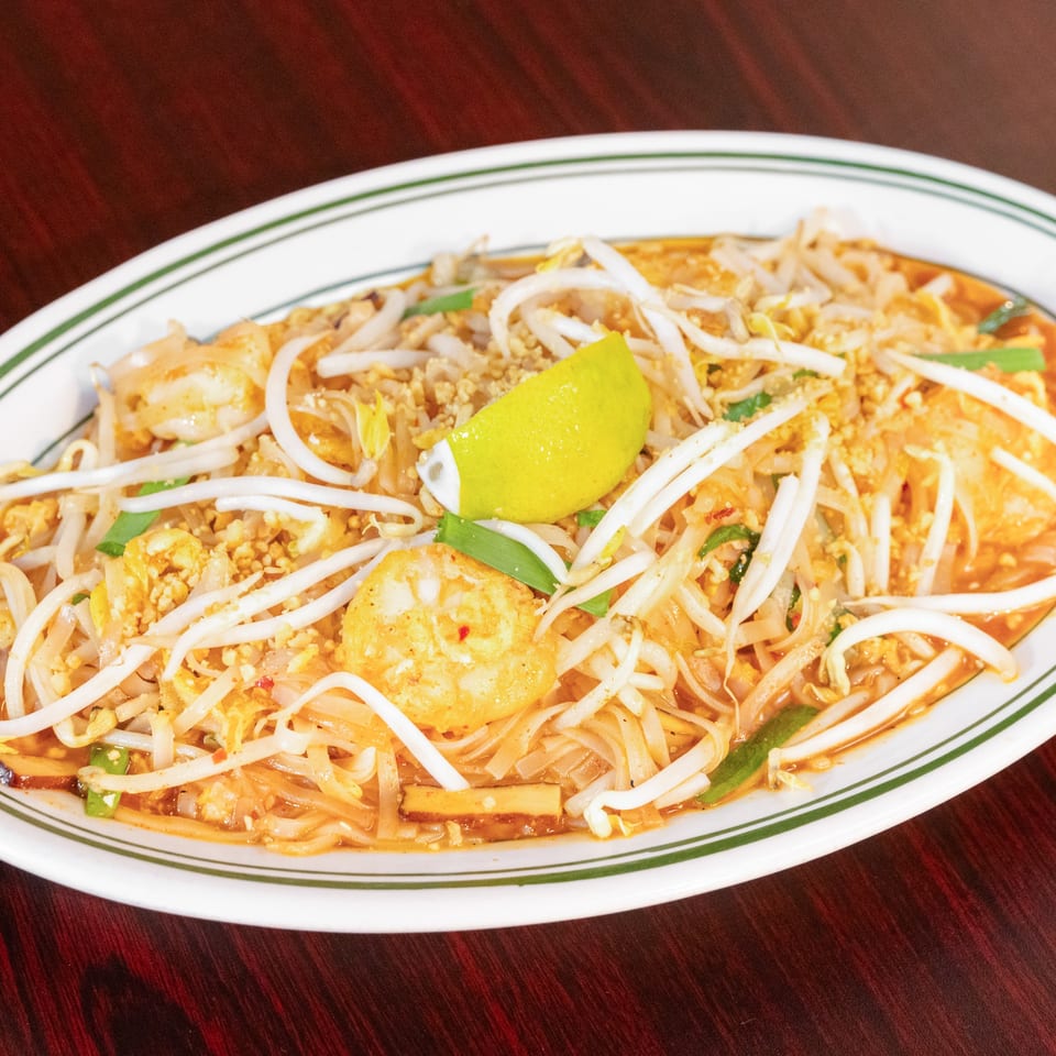 Pad Thai noodles with shrimp, bean sprouts, crushed peanuts, green onions, and lime on a white oval plate.