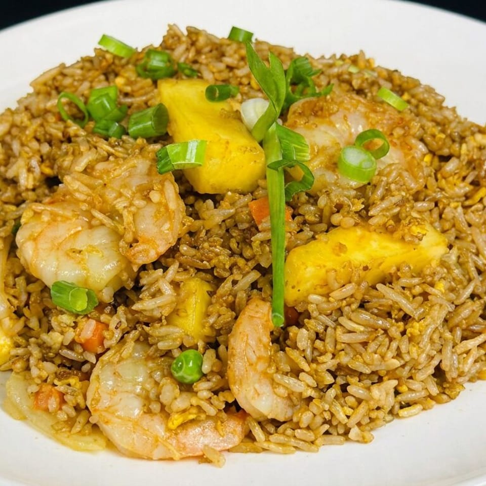 Plate of fried rice with shrimp, chicken, vegetables, pineapple chunks, and green onions.