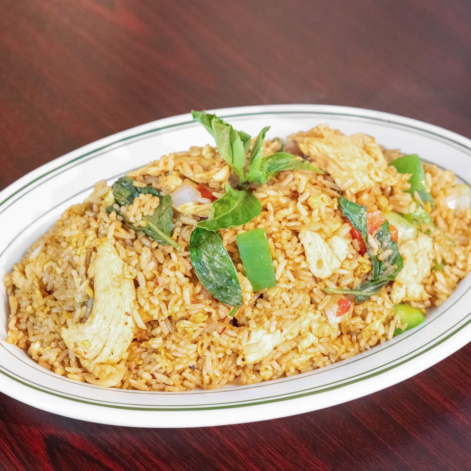 Plate of fried rice with chicken, vegetables, and fresh basil garnish on a wooden table.
