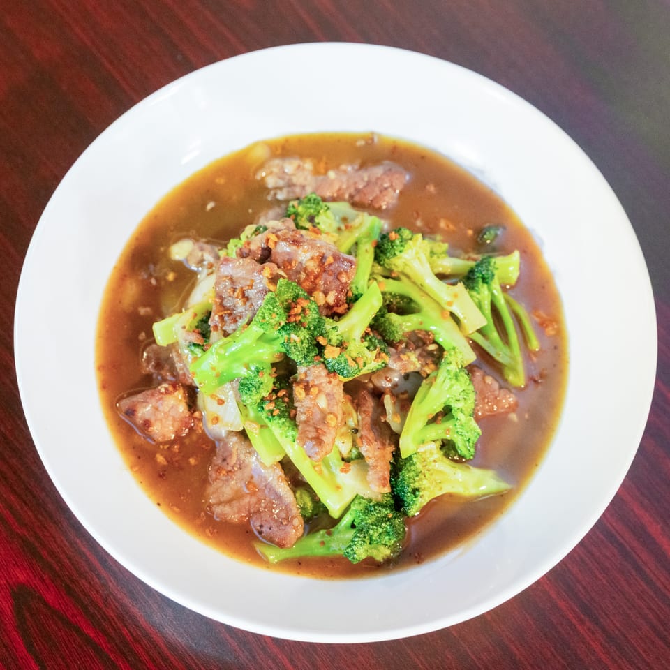 Sliced beef and bright broccoli served in a glossy brown sauce on a white plate atop a dark wooden table.
