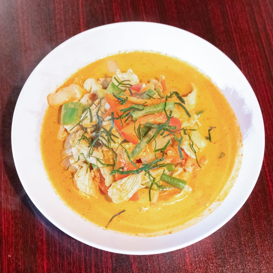 Thai-style chicken curry with vegetables and shredded herbs in a creamy orange sauce, served on a white plate.