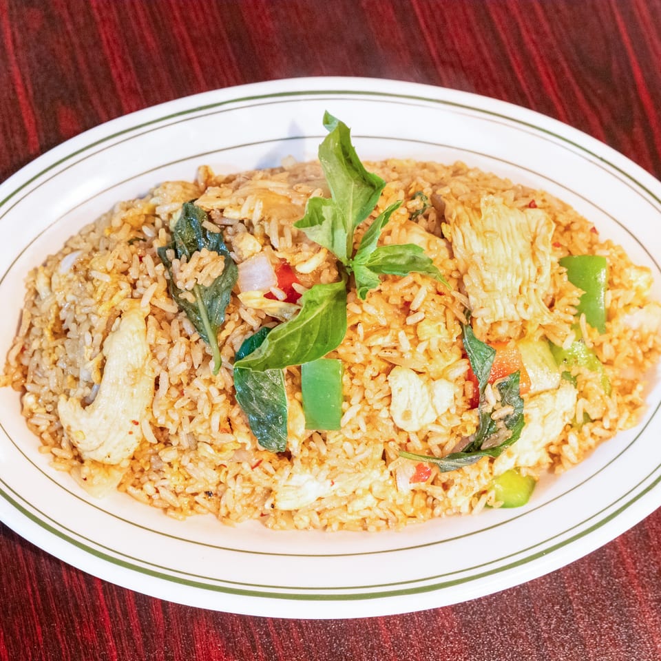 Plate of fried rice with chicken, vegetables, and fresh basil on a white oval dish.