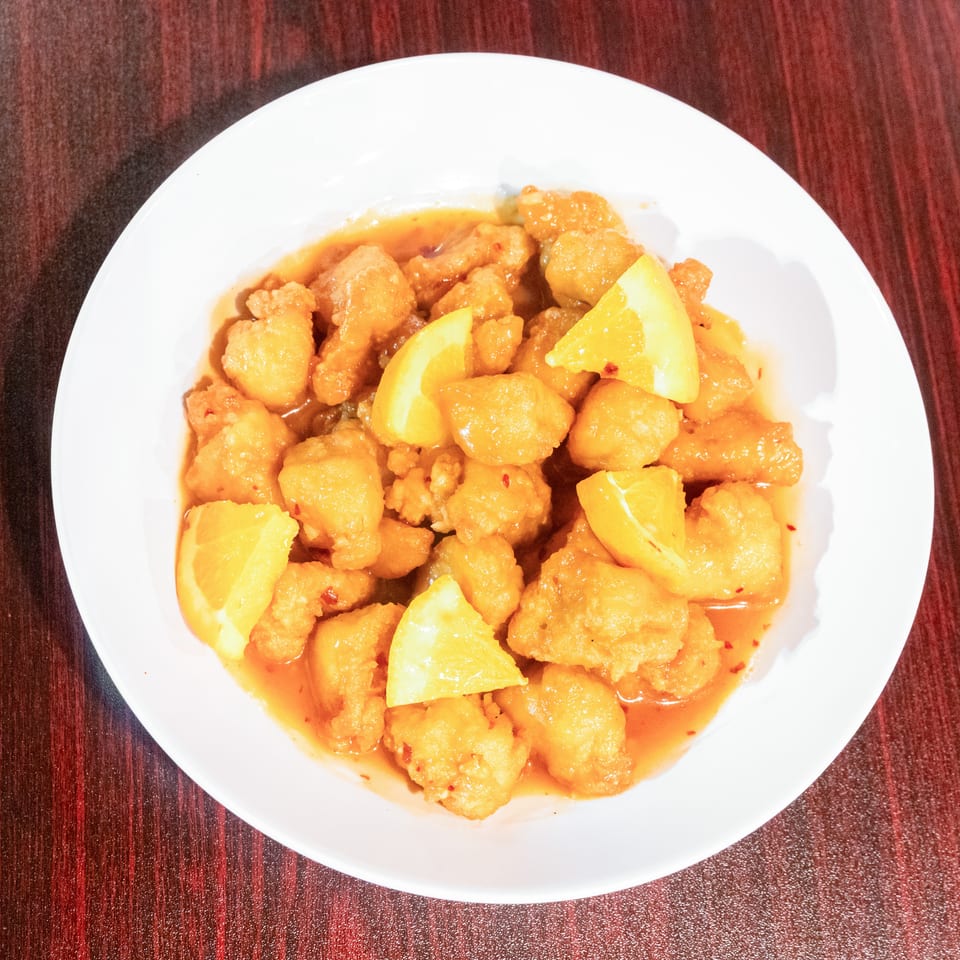 Plate of crispy golden chicken pieces in orange sauce, garnished with fresh lemon wedges on a dark wooden table.
