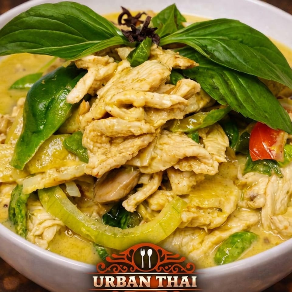 Bowl of creamy Thai green curry with sliced chicken, vegetables, basil leaves, and red chilies.