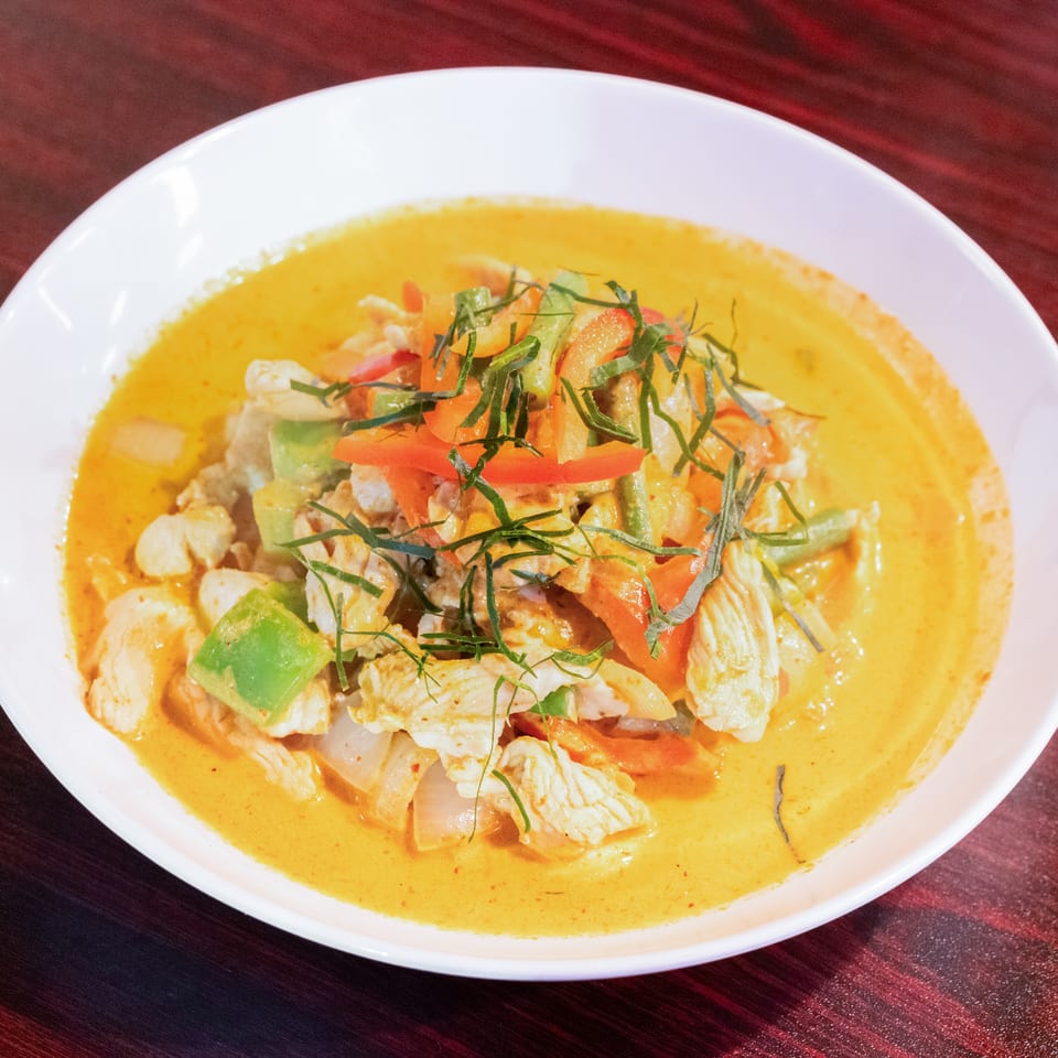 Thai-style yellow curry with chicken, vegetables, and shredded herbs served in a white bowl.